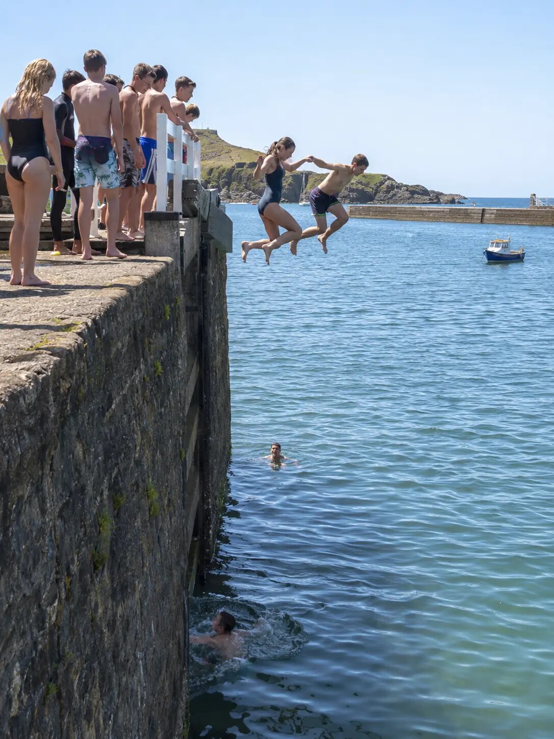 Teenagers jumping from the stone wall at Bude Canal sea lock with the breakwater beyond