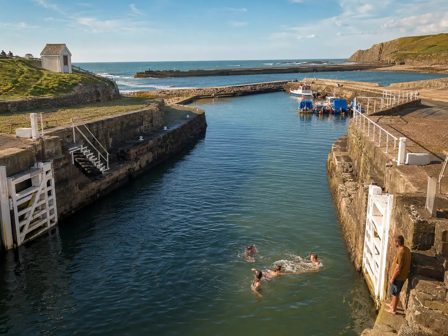 Swimmers in Bude Canal sea lock looking towards the harbour breakwater and Atlantic