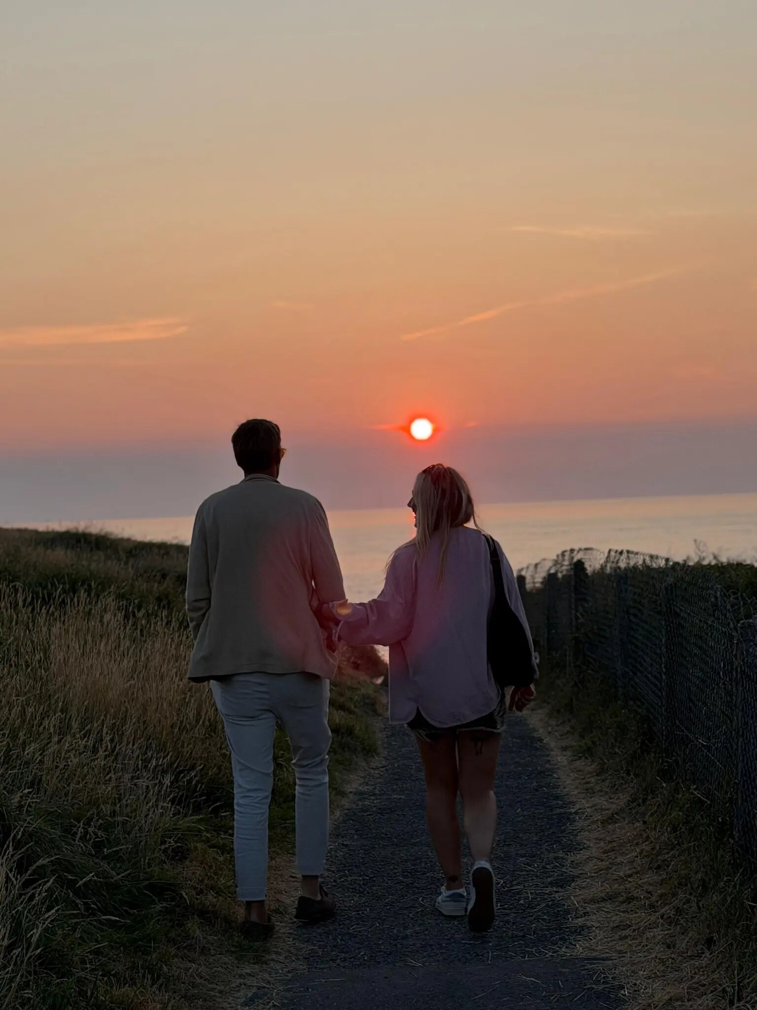 Two people walking towards the sunset on the coast near Bude