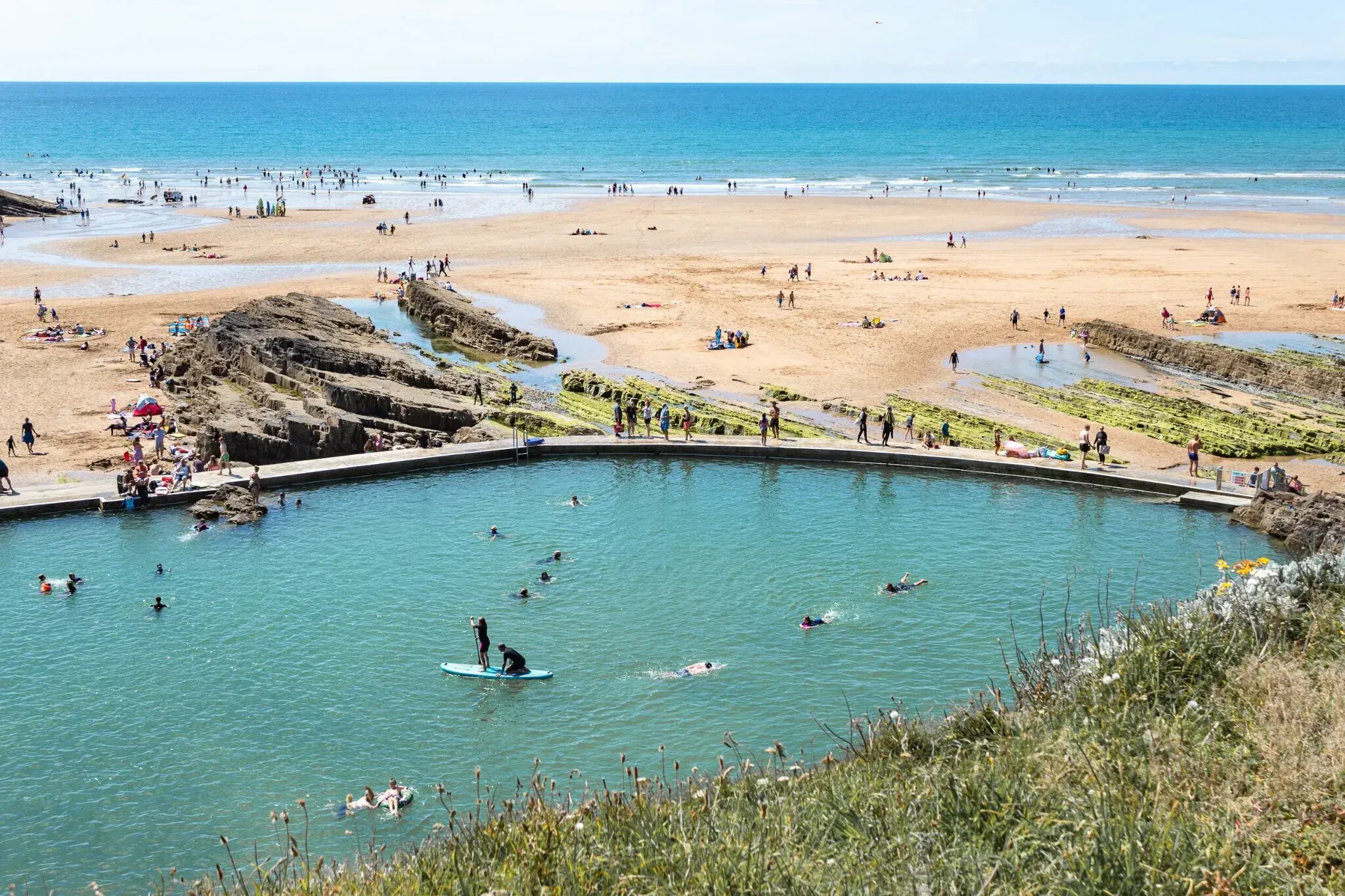 Swimmers and paddleboarders in Bude Sea Pool beside Summerleaze Beach