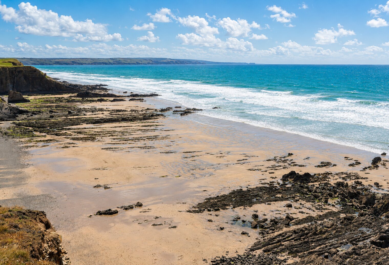 Sunny elevated view over Northcott Mouth Beach, its rock shelves and the bright blue Atlantic