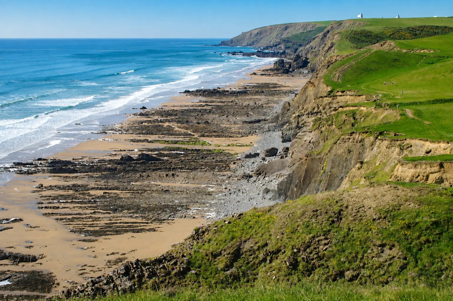 Sunny elevated view along Sandymouth Bay's dramatic cliffs, rock shelves and blue Atlantic shoreline
