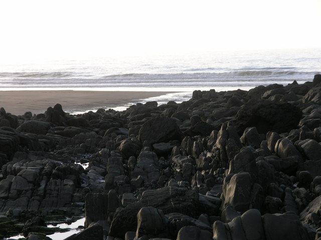 Dark reef rocks and the stream mouth meeting the Atlantic at Duckpool