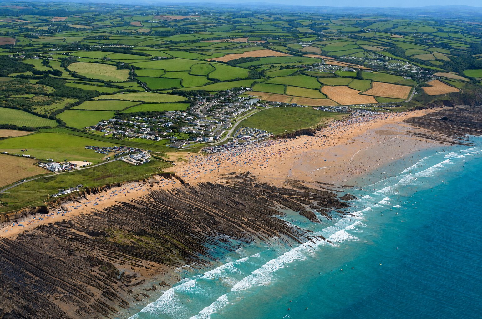 Sunny aerial view of families, swimmers and surfers enjoying Widemouth Bay